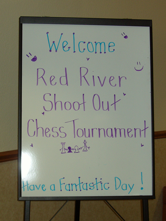 Photo of a white board with the words WELCOME RED RIVER SHOOTOUT CHESS TOURNAMENT HAVE A FANTASTIC DAY